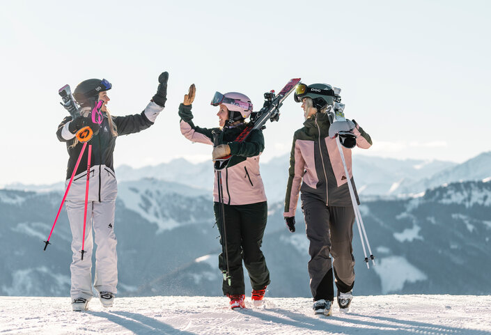 Sonnenskilauf im Skicircus Saalbach Hinterglemm Leogang Fieberbrunn, drei Personen gehen über die Sie, zwei klatschen ein | © saalbach.com, Christoph Johann