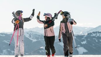 Sonnenskilauf im Skicircus Saalbach Hinterglemm Leogang Fieberbrunn, drei Personen gehen über die Sie, zwei klatschen ein | © saalbach.com, Christoph Johann