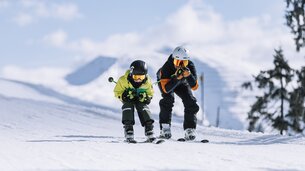 Familienurlaub in Skicircus Saalbach Hinterglemm Leogang Fieberbrunn, ein Vater und sein Sohn rasen Schuss die Piste hinunter | © saalbach.com, Mia Knoll
